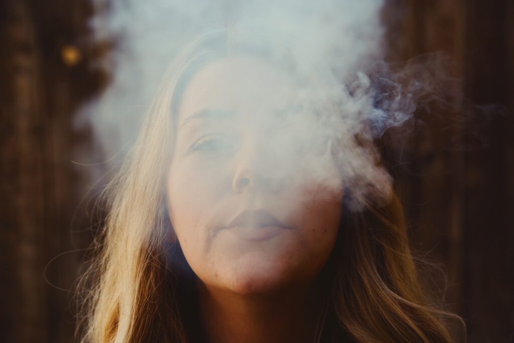 Woman exhales while dry herb vaping in the woods.