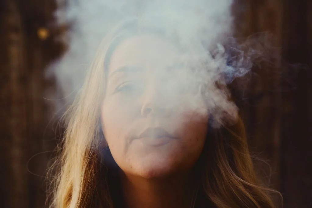 A woman exhales vapor in the woods