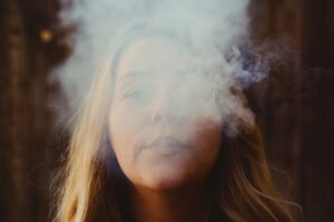A woman exhales vapor in the woods